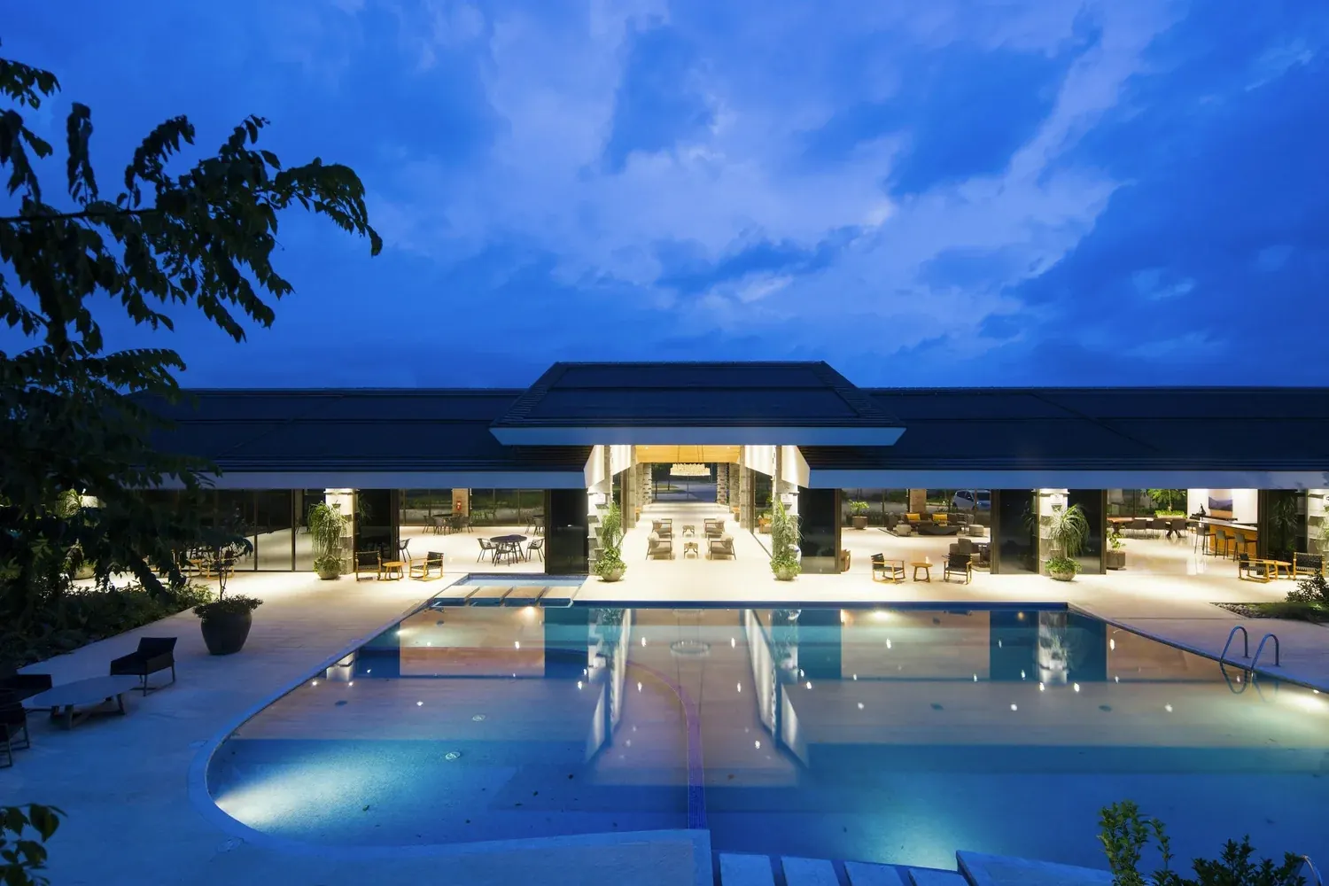 A luxury hotel courtyard and pool at dusk, with the lobby lit warmly behind it.